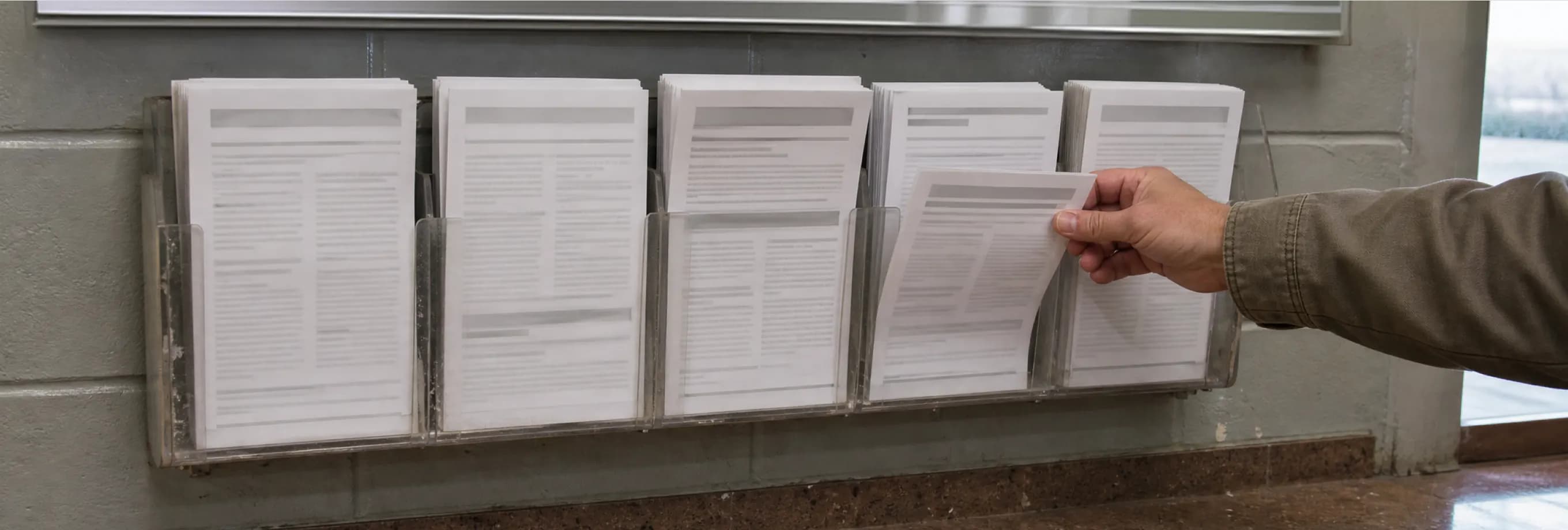 A wall rack of printed information leaflets in a courthouse lobby, a hand taking one from a middle slot