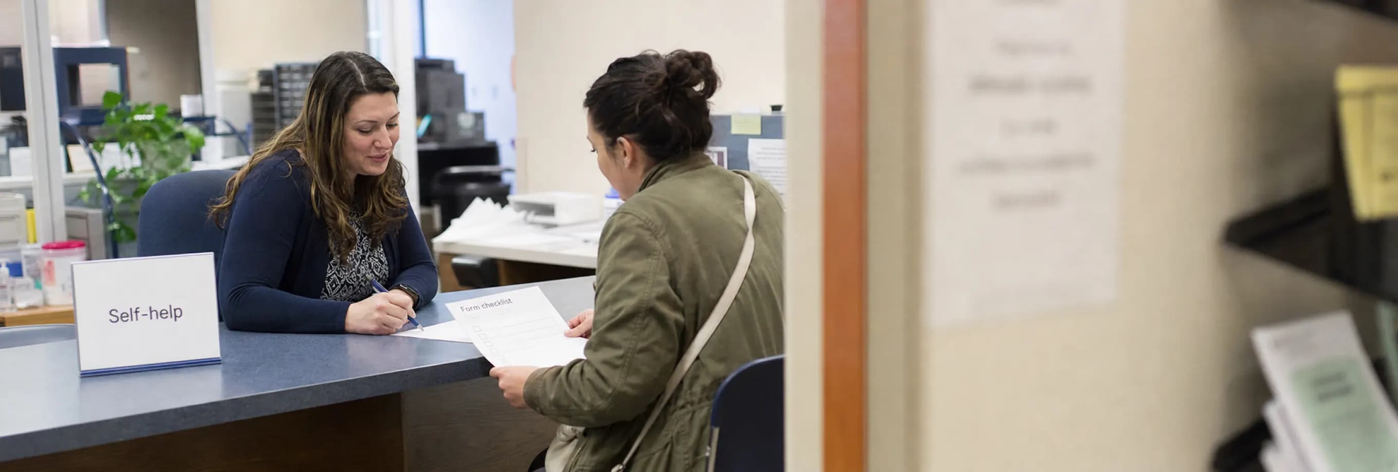 A staff member and a self-represented filer reviewing a form checklist across a self-help counter