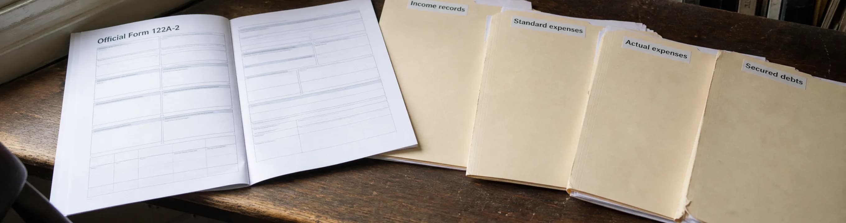 Official Form 122A-2 open beside folders labeled income records, standard expenses, actual expenses and secured debts