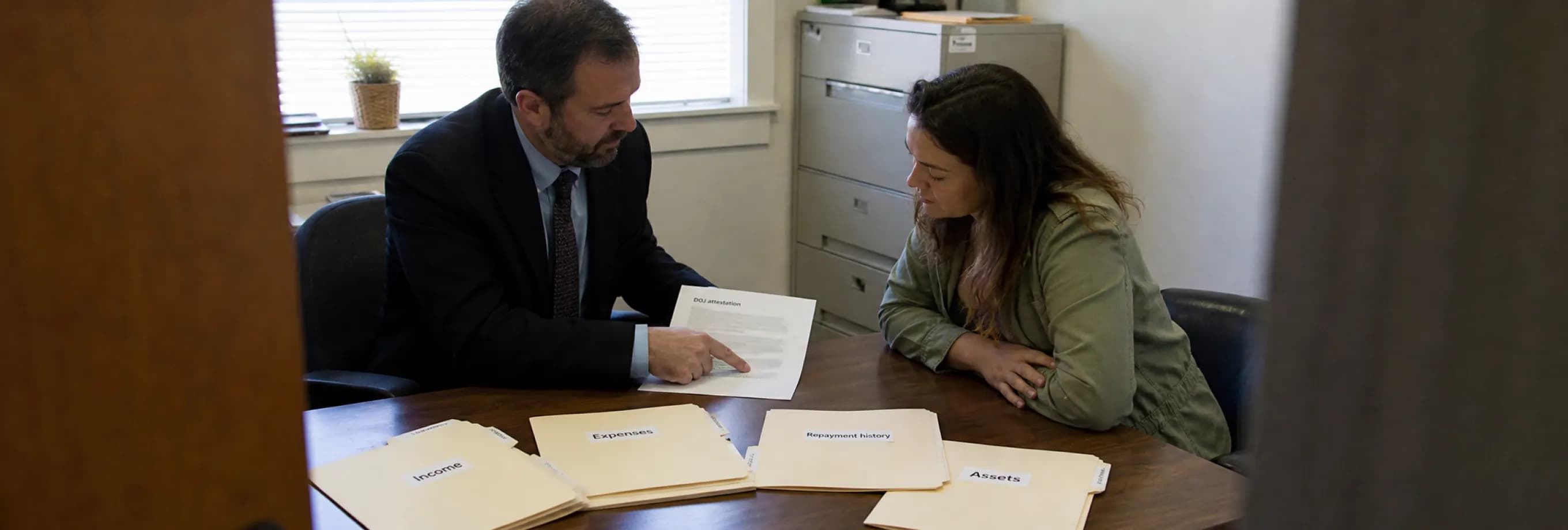 Two people reviewing the attestation form beside separate folders of income, expense, repayment and asset records